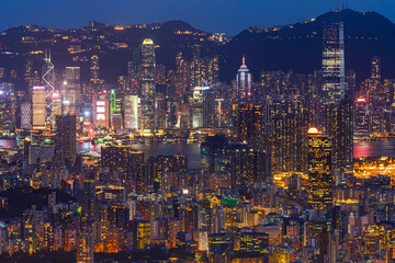 Obraz premium Hong Kong city view from above with modern buildings and towns lit up at night across island. Light hits buildings which creating focal point in city with modern buildings and road with traffic light.