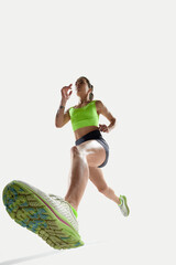 Low angle shot of female runner in bright green top and black shorts, stepping forward with powerful stride. Concept of sport, competition, active lifestyle, perspective, strength, power.