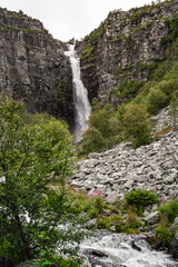 Njupeskär Waterfall plunges dramatically down a rocky landscape in Fulufjället National Park, surrounded by lush greenery and rocky terrain, showcasing nature's beauty in Dalarna Sweden