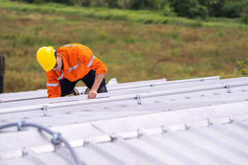 Worker in an orange safety uniform and helmet carefully inspecting a metal rooftop under natural daylight. Depicts diligence, precision, and professional commitment in construction and maintenance.