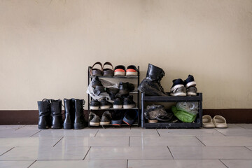 Many pairs of shoes boots, sandals, sneakers on a small old shelf at front door entrance outside room for rent apartment.