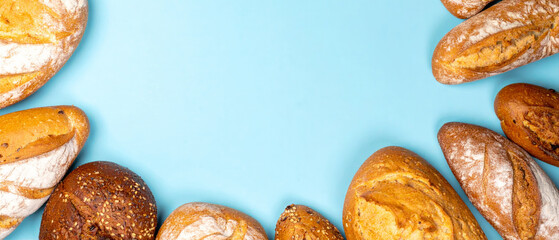 Different types of bread loaves arranged on a light blue surface, creating a frame with empty space in the center