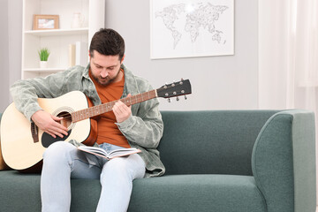 Relaxing hobby. Man with guitar and book on sofa at home