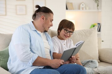 Father and his son reading book together on sofa at home