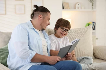Zelfklevend Fotobehang Father and his son reading book together on sofa at home © New Africa