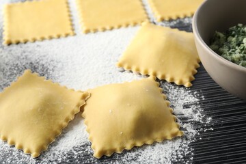 Uncooked ravioli, stuffing and flour on wooden table, closeup