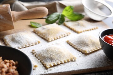 Uncooked ravioli, rolling pin, bolognese, sauce and basil on table, closeup