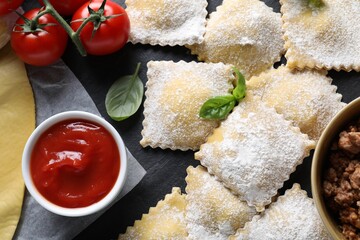 Uncooked ravioli, bolognese, sauce, tomatoes and basil on black table, flat lay