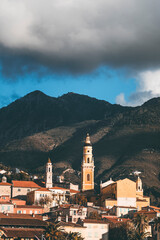 vertical shot of the old town of mentone, in french riviera, with blue sky and high contrast light, view of the bell tower and dark mountains background
