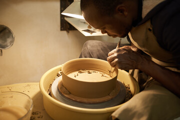 African ceramist working a bowl with a handle maker tool in a studio