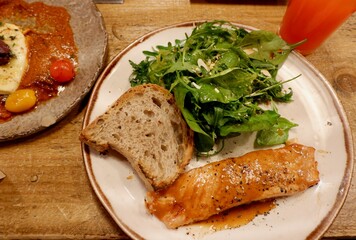 salmon fillet garnished with spices is plated alongside a vibrant salad of mixed greens and slice of crusty bread