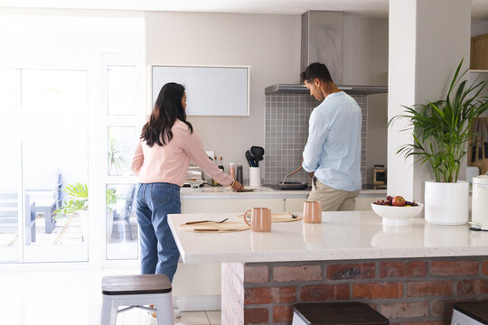 Diverse couple making breakfast in modern kitchen, using cooking pot and coffee mugs