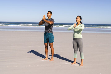 Couple practicing yoga on beach, standing in prayer pose, enjoying morning sun