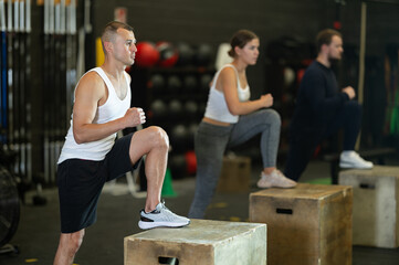 Determined young guy stepping on box in sports hall during crossfit workout