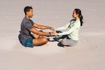 Fototapeta premium Couple practicing yoga on beach, holding hands and meditating together peacefully