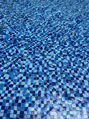 Pool floor background with gently wavy water and small checkered pattern ceramic mosaic floor in blue