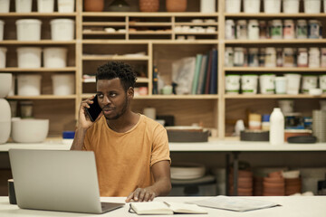 Fototapeta premium African ceramics studio manager talking on a phone and using a laptop