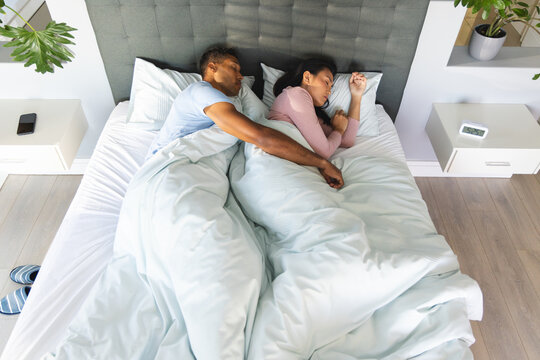 Couple sleeping peacefully in bed, embracing under cozy blankets at home