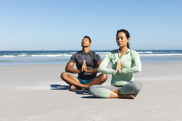Couple meditating on beach, practicing yoga with serene ocean backdrop