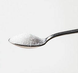 A small pile of granulated white sugar sits atop a metal spoon, against a plain white background