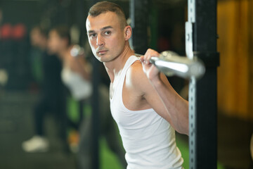 Athletic young adult man participating in intense group training in gym, performing exercises with...