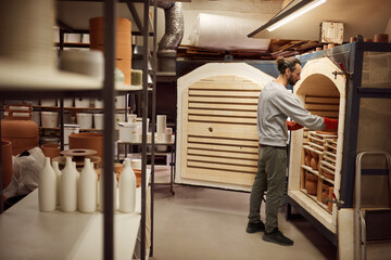 Ceramist removing earthenware from a workshop kiln