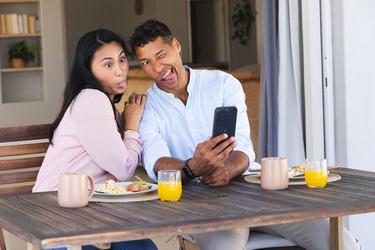 Couple making funny faces taking selfie during breakfast on patio table