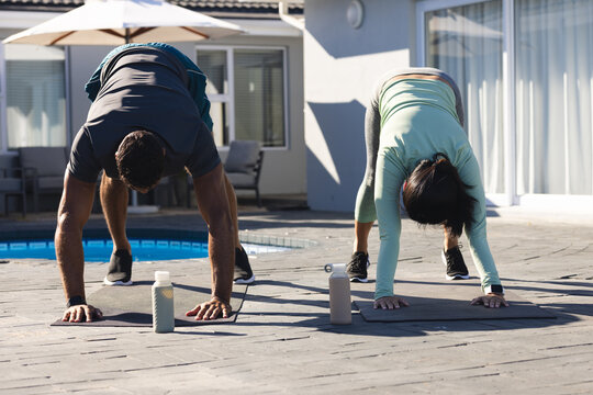 Couple exercising outdoors, practicing yoga poses by poolside on sunny day