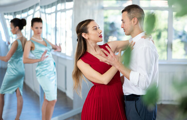Guy and girl in stage costumes, under guidance of mentor, practice tango in choreographic studio....