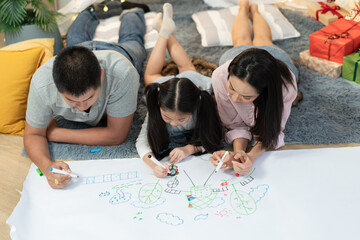 Happy Asian family drawing on paper together. Daughter with parent lying on floor and playing...