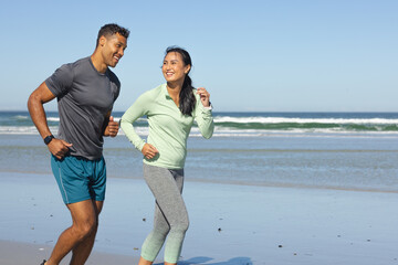 Fototapeta premium Couple jogging on beach, smiling and enjoying sunny day by ocean, copy space