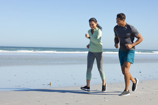 Couple jogging on beach, enjoying morning exercise and fresh ocean breeze