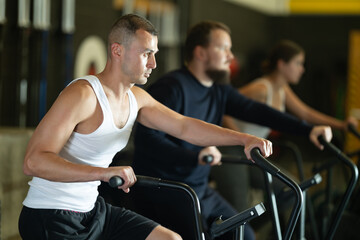 Willing young man engaged in air-bike workout in exercise room during weight training classes