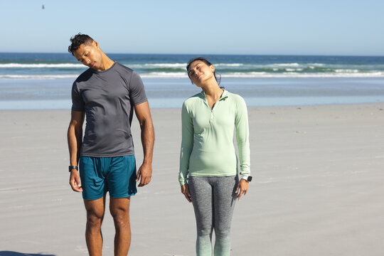 Couple stretching necks on beach during morning exercise routine, enjoying fresh air
