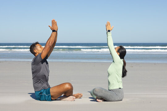 Asian couple practicing meditation on beachside, embracing sunlight and ocean peace