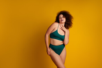 Confident plus size woman modeling green lingerie on a bold yellow background, celebrating body diversity, self confidence