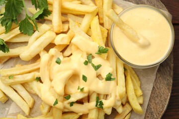 Delicious cheese sauce in bowl, French fries and parsley on table, top view