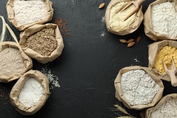 Different types of flour in paper bags on black table, flat lay. Space for text