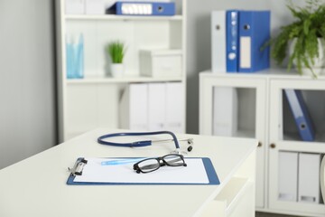 Doctor's workplace. Stethoscope, clipboard, pen and glasses on white table in medical office