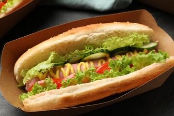 Tasty hot dog with vegetables on black table, closeup