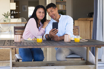 Smiling couple enjoying breakfast and taking selfie at home dining table