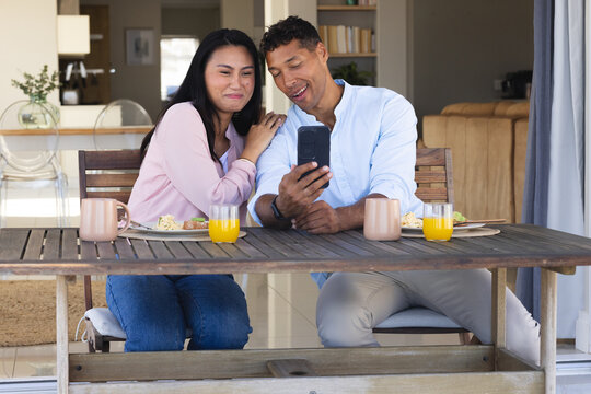 Smiling couple enjoying breakfast and taking selfie at home dining table