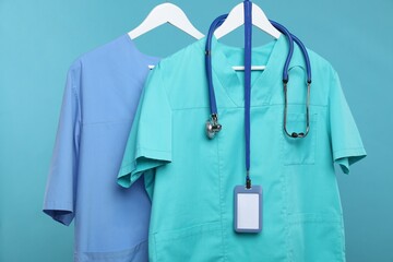 Medical workers uniforms with stethoscope and badge on hangers against blue background