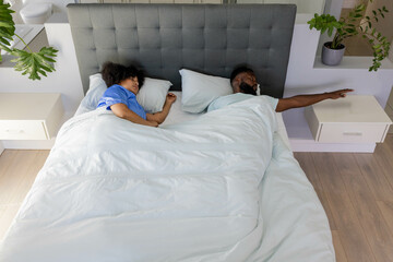 African American couple sleeping peacefully in bed, reaching for morning alarm