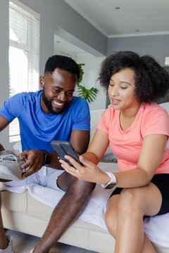 Couple relaxing at home, smiling and looking at smartphone together on couch