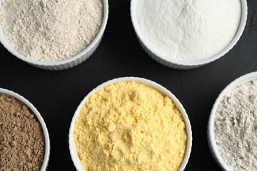 Different types of flour in bowls on black table, flat lay