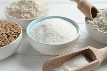 Different types of flour in bowls and scoops on white wooden table, closeup