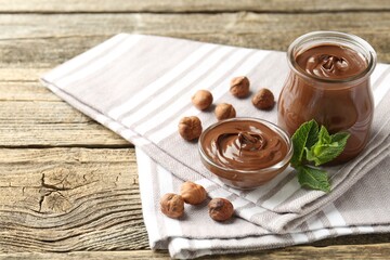 Tasty chocolate spread, hazelnuts and mint on wooden table, closeup