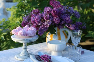 Beautiful lilac flowers, zephyrs, plates, cutlery, glasses and candle on table in garden