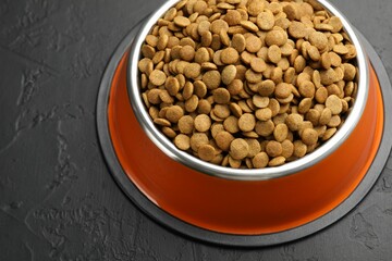 Dry pet food in feeding bowl on black textured background, closeup